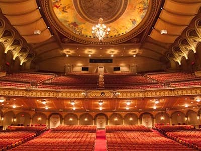 view of an empty concert hall take from the stage. The ceilings are ornate and gold, while the seats are red velvet.