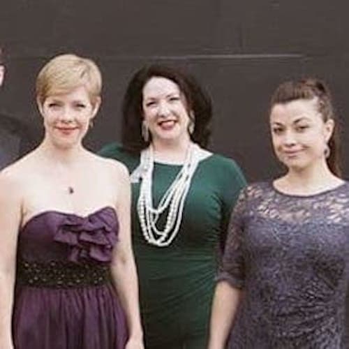 Eight people in evening wear standing and facing the camera. The women are all wearing formal dresses.